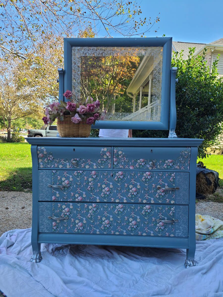 A blue dresser with flowers on it and a mirror