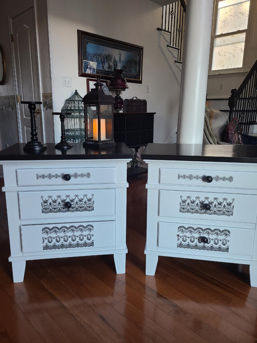 Two white and black nightstands with a candle in the middle.