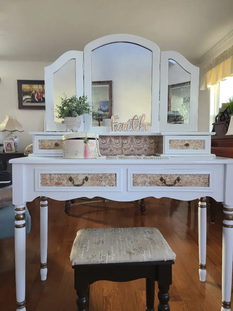 A white vanity with three mirrors and two drawers.