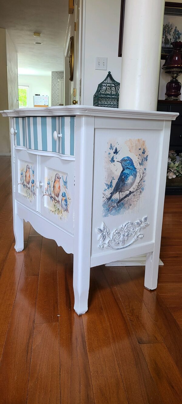 A white dresser with bird and butterflies painted on it.