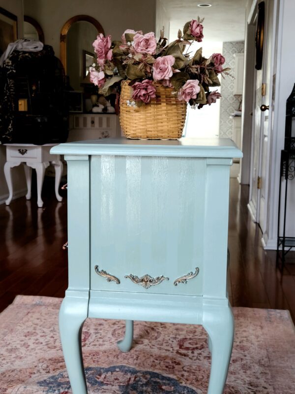 A blue nightstand with flowers in the middle of it.