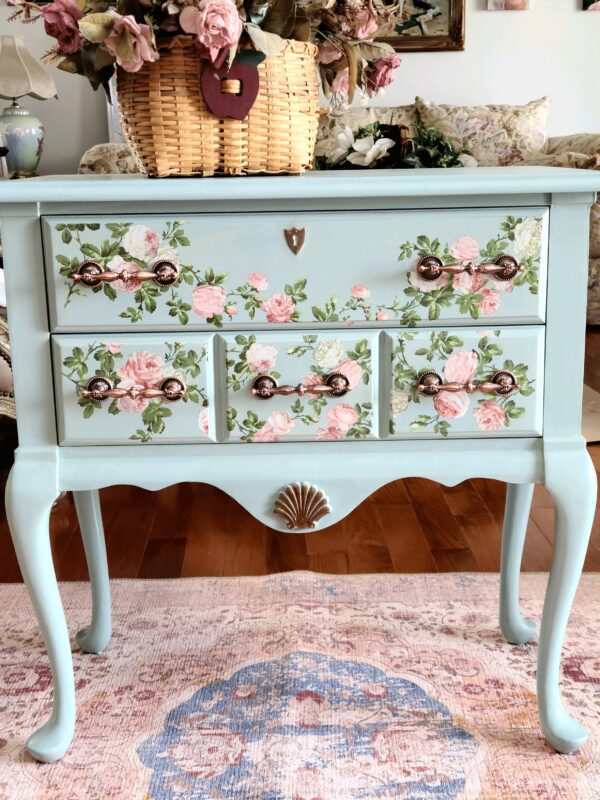 A blue dresser with pink and white flowers on it.