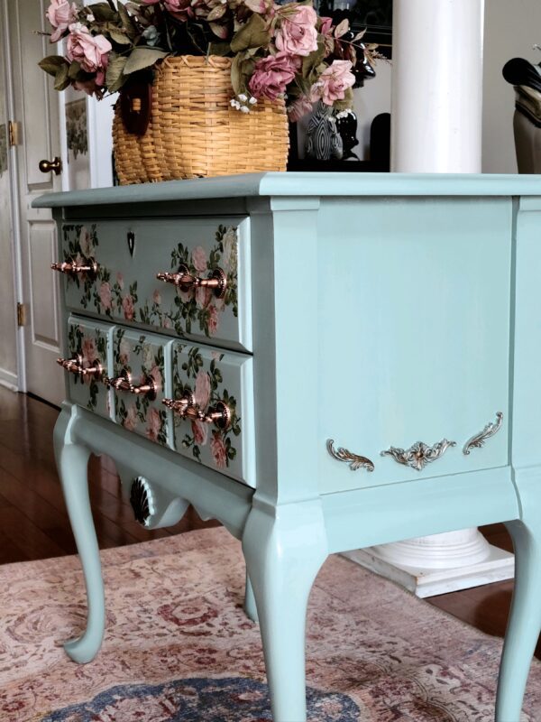 A blue dresser with floral designs on it.