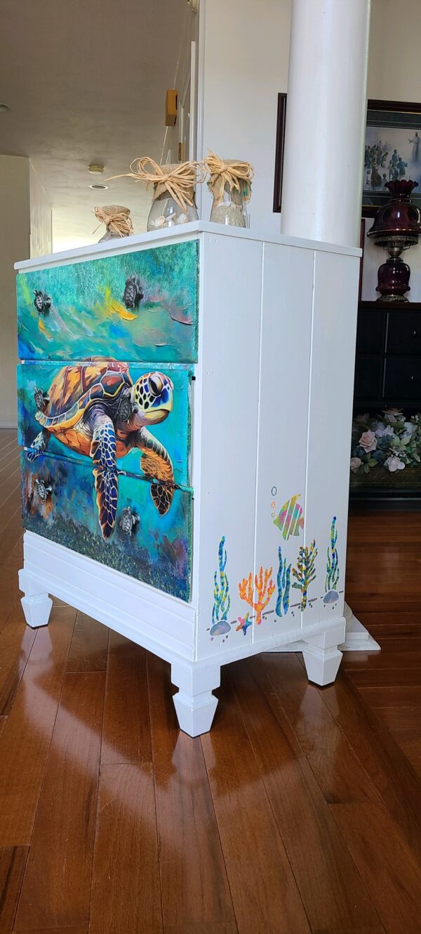 A white dresser with sea turtle painting on the side.